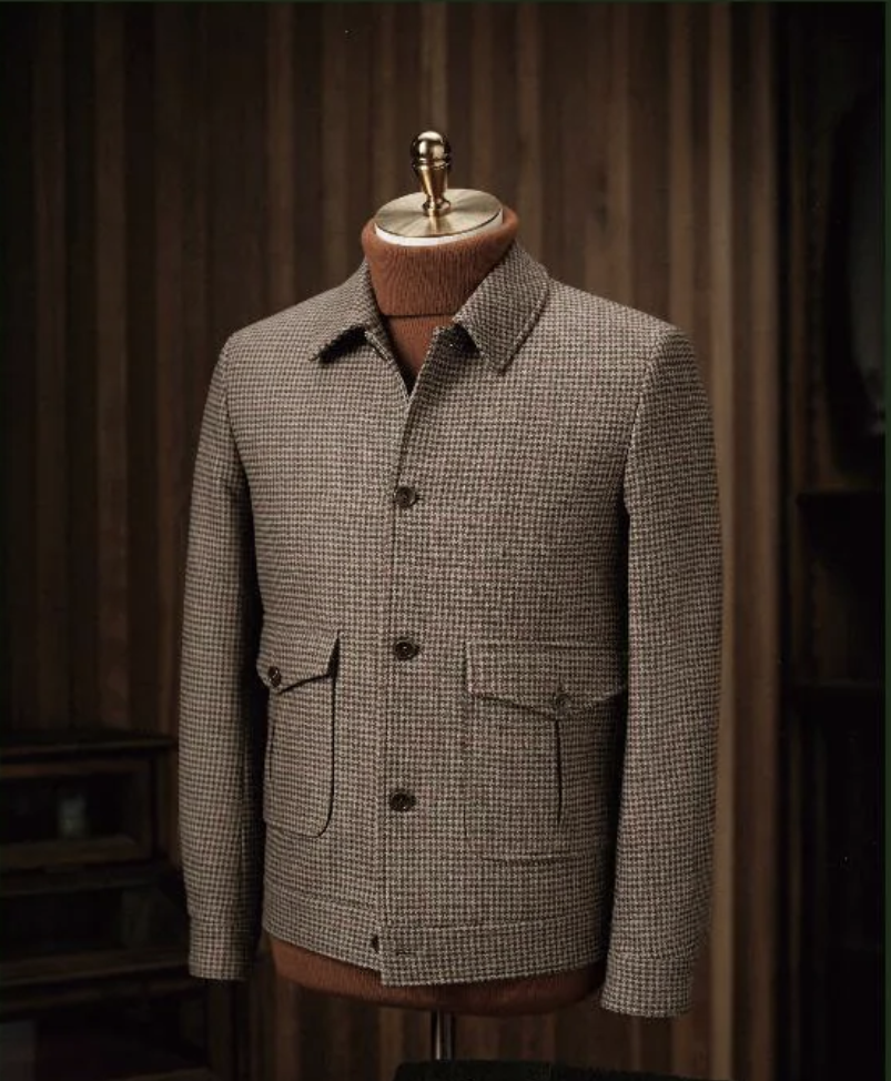 with a collar and dark brown buttons on the front sleeves, displayed on a mannequin against a wooden background.