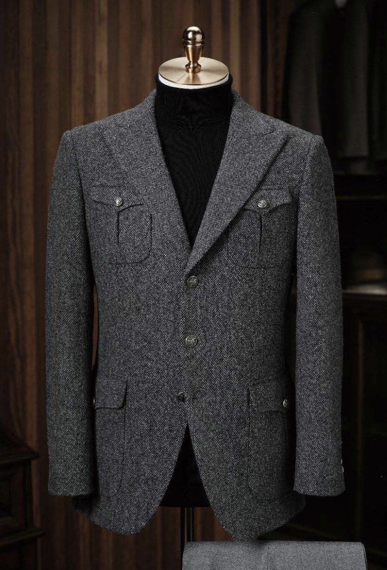 A charcoal tweed jacket and grey wool trousers displayed on a mannequin, featuring a slim fit with button details, pockets, and a peak lapel.