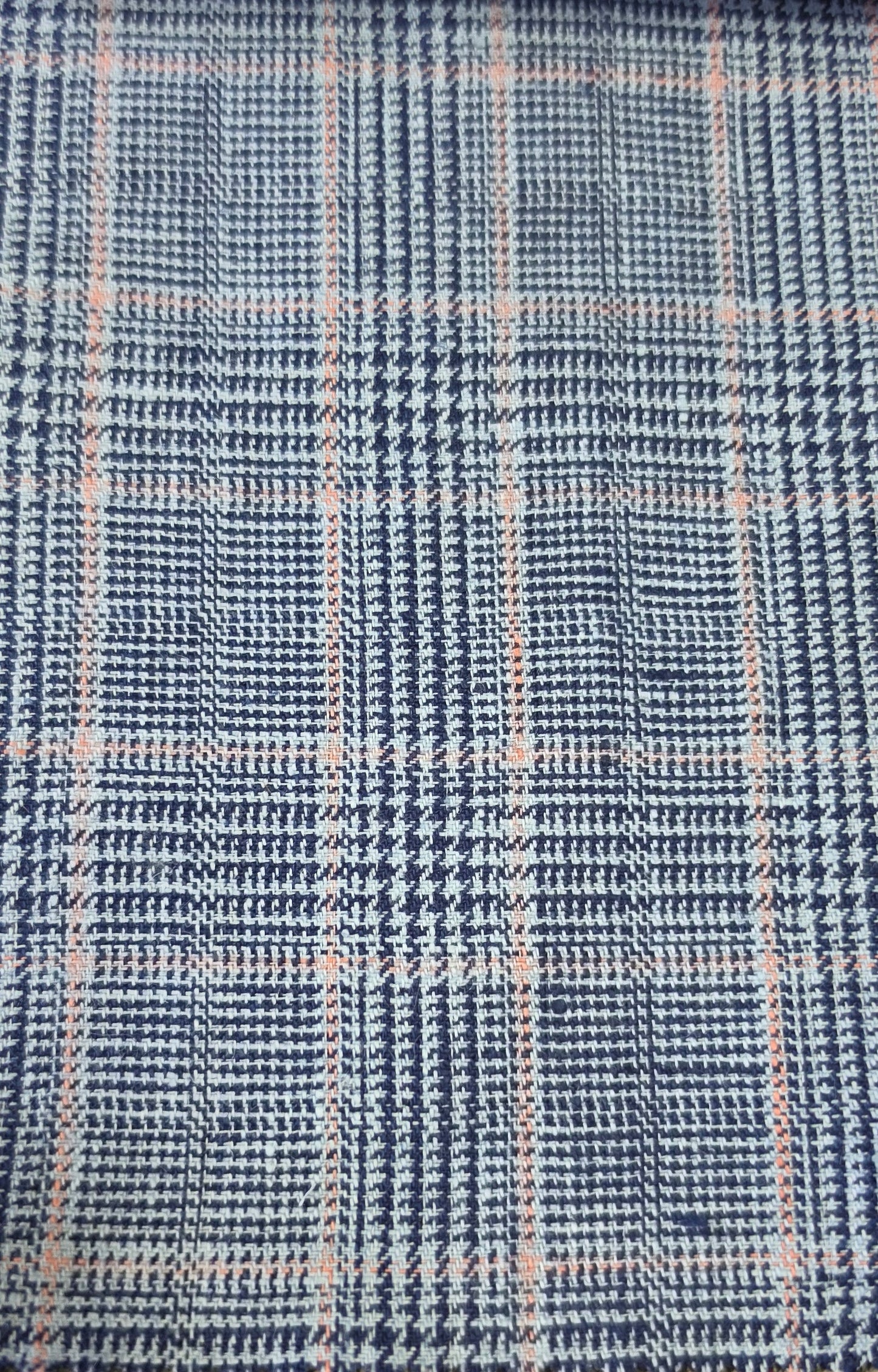 A close-up of a woven fabric with a blue and white houndstooth pattern overlaid with a light pink plaid grid.