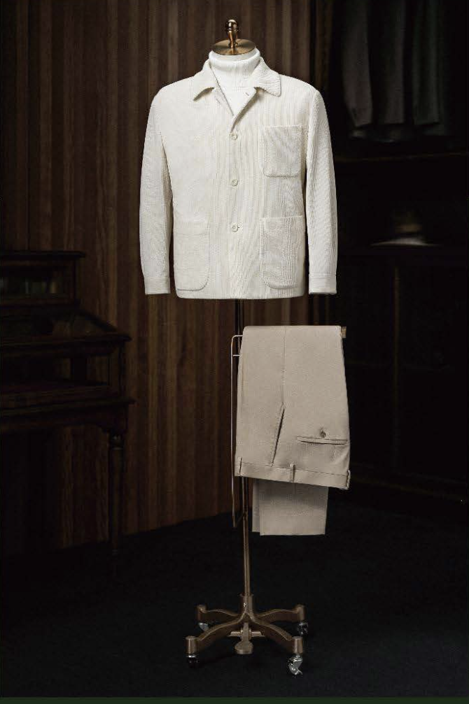 A white cord casual jacket and beige trousers displayed on a mannequin, with the jacket featuring a high shirt collar, three-button fastening, and round patch breast pocket, and the trousers having a plain waistband and front pockets.