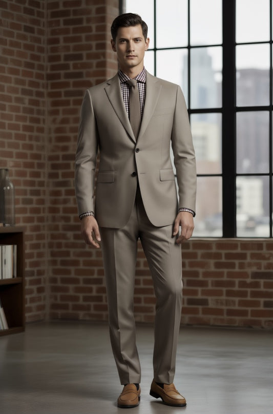 Man wearing a beige suit standing in a room with brick walls and large windows.
