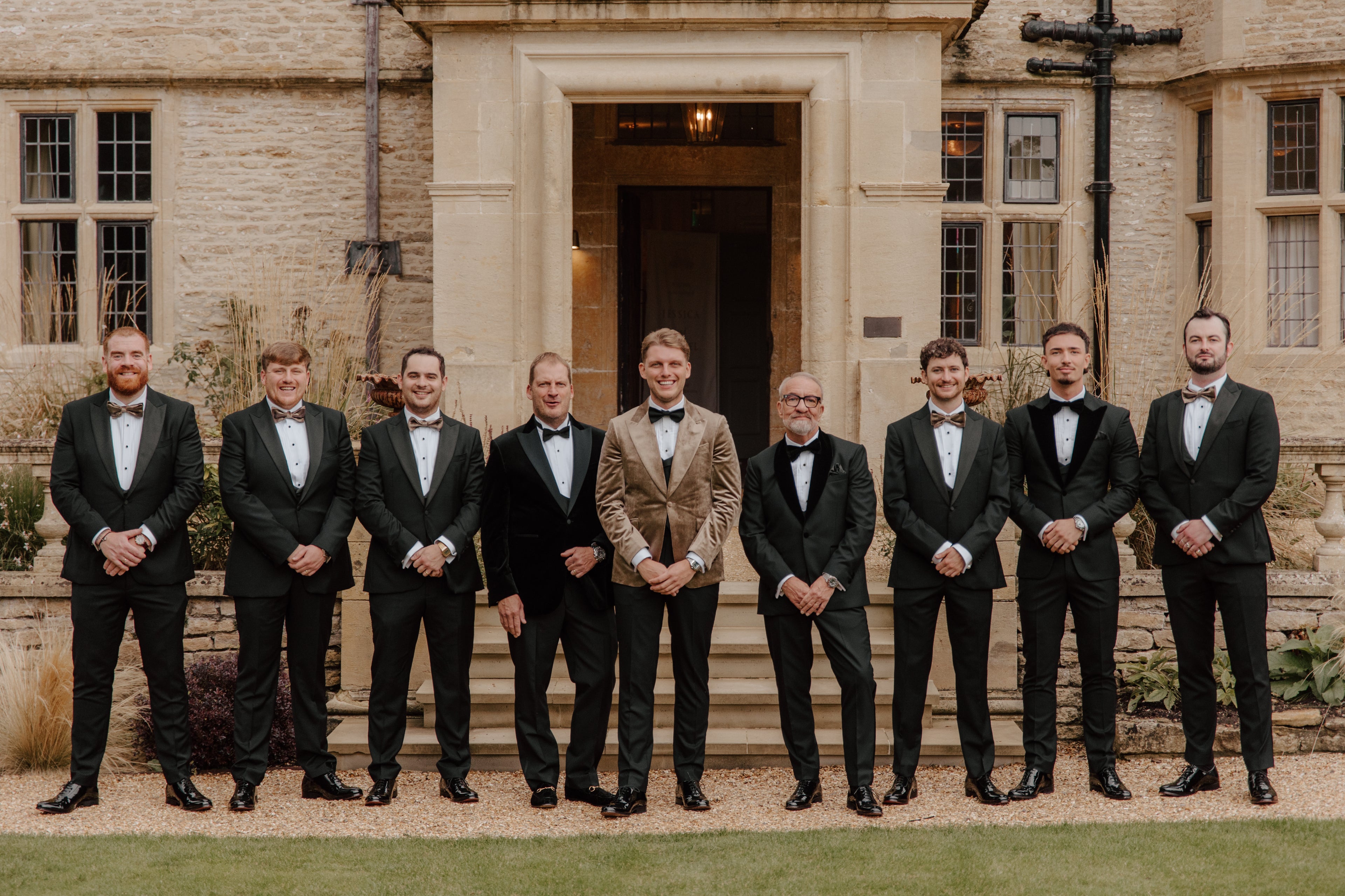 Groom and groomsmen in bespoke black tuxedos and bow ties at elegant wedding venue - A Hand Tailored Suit wedding collection