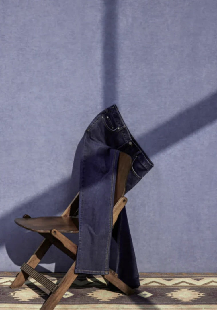 Blue jeans draped over a wooden chair against a blue wall