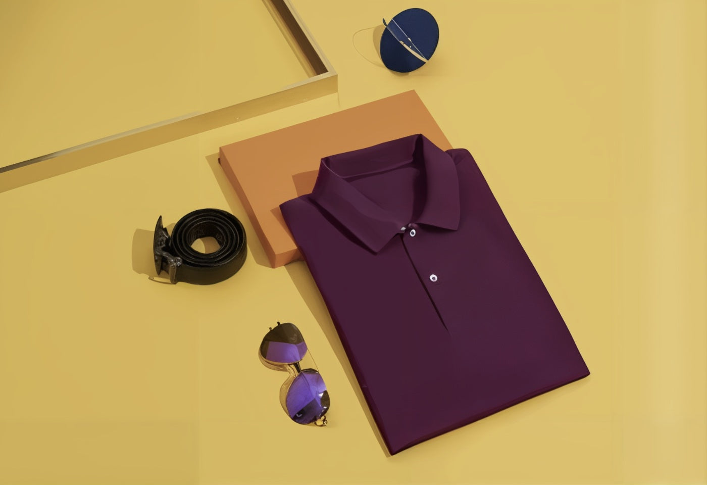 Cerise polo shirt, black belt, and sunglasses on a yellow surface