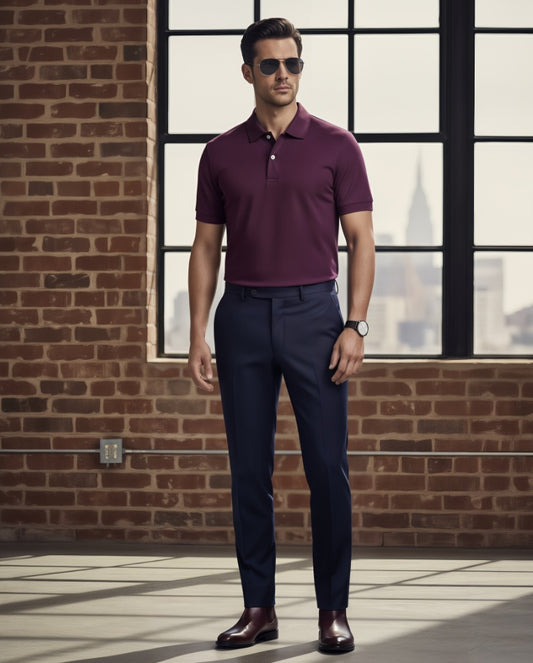 Man wearing a Cerise polo shirt and navy pants standing in front of a brick wall with large windows.