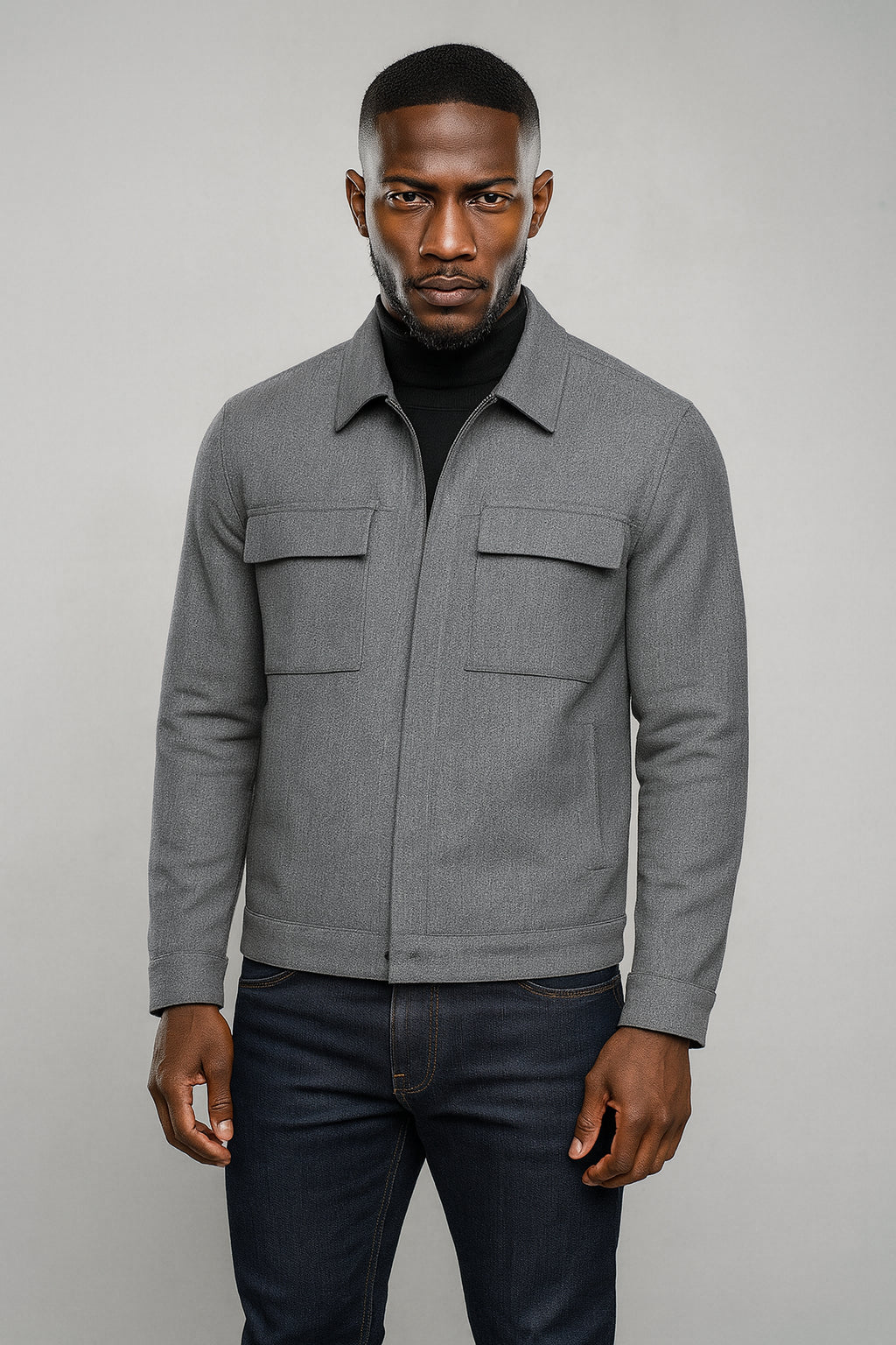 Man wearing a gray jacket and dark jeans against a plain background