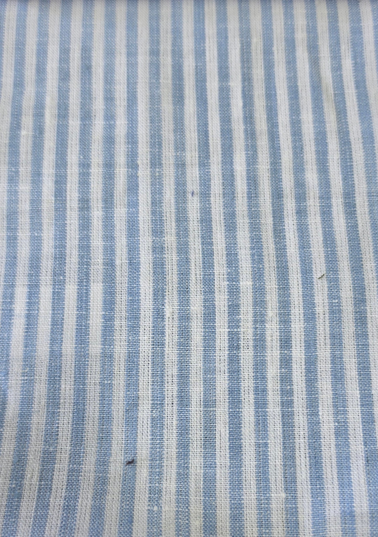 A close-up of a woven fabric with vertical stripes in light blue and off-white, showing a textured linen-like weave.