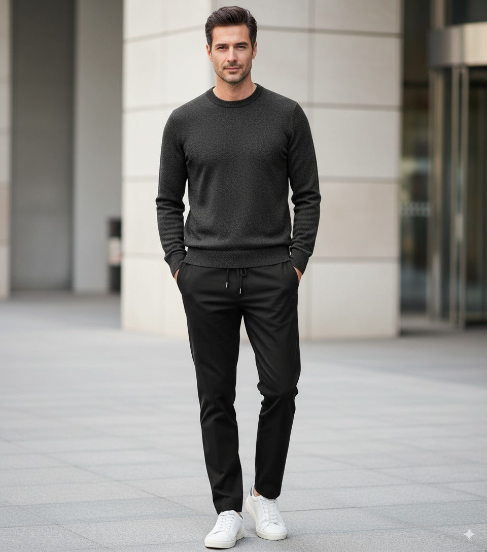 Man wearing a dark gray sweater and black pants with white shoes, standing in front of a building.