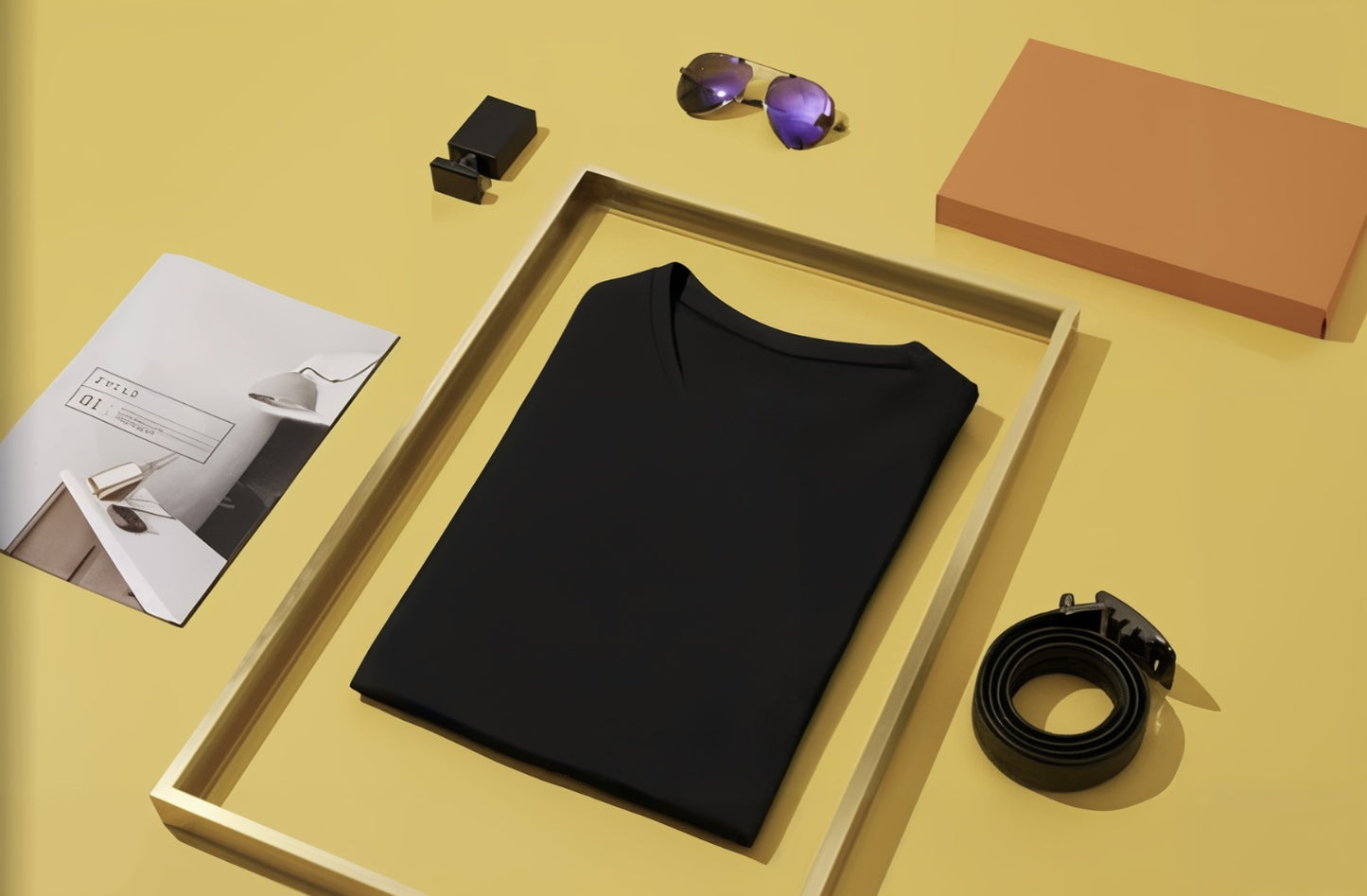 Black t-shirt on a yellow surface with accessories including sunglasses, a box, and a belt.