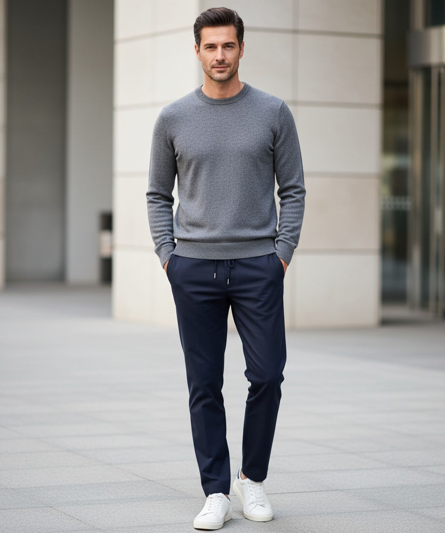Man wearing a gray sweater and navy pants standing in front of a building.