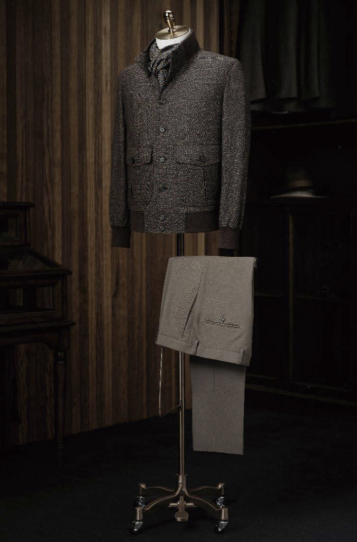 Mannequin wearing a gray textured jacket with a matching scarf, standing next to a folded gray garment on a stand against a dark background.