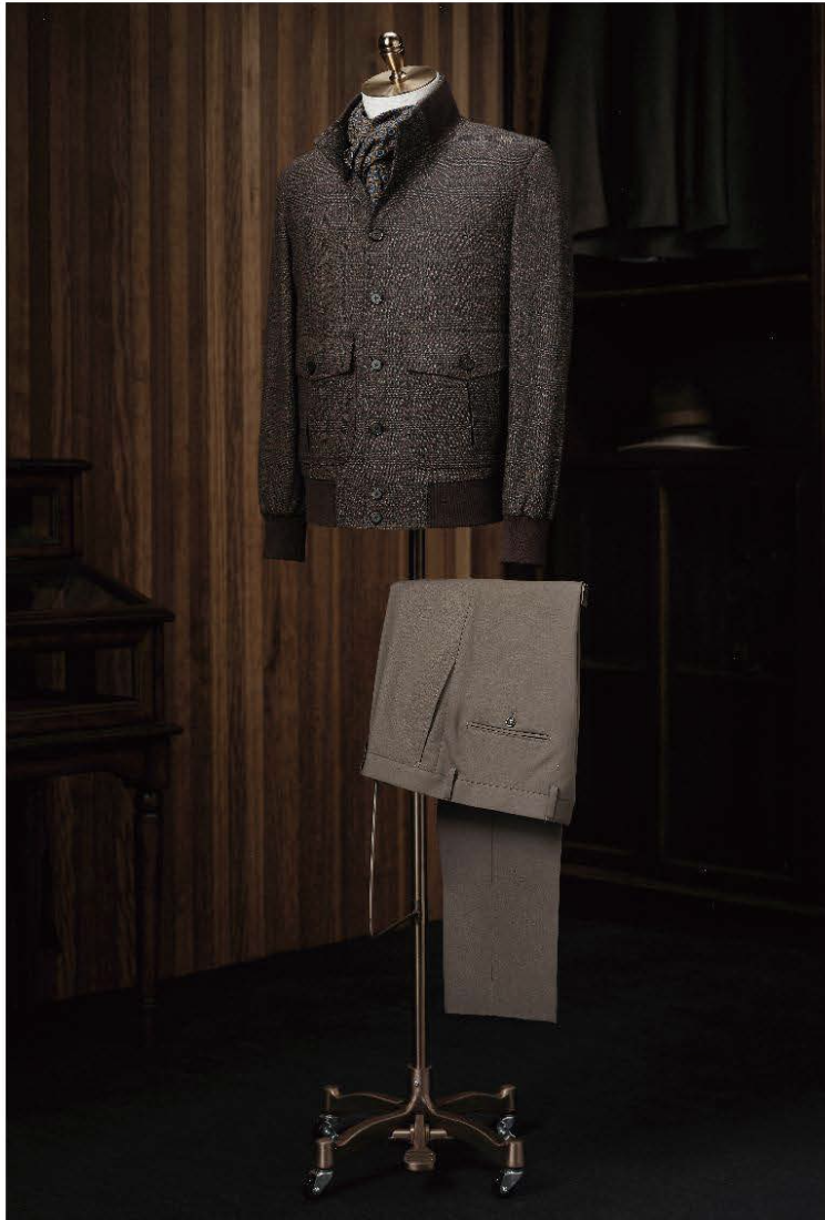 A brown check casual jacket and brown trousers displayed on a mannequin against a background of a wood-paneled room with dark brown furniture.