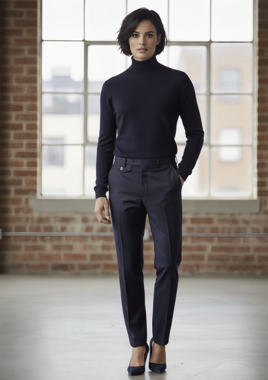 Woman wearing a Navy turtleneck and dark pants standing in a room with brick walls and large windows.