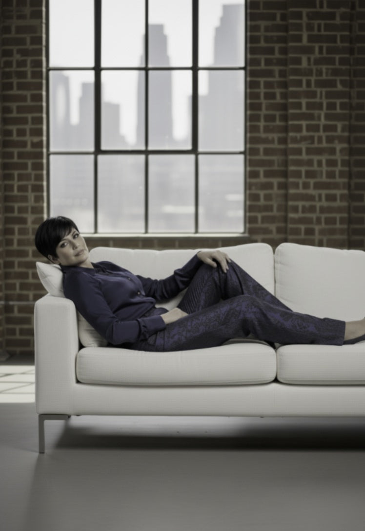 Person sitting on a white couch in a room with large windows and brick walls.