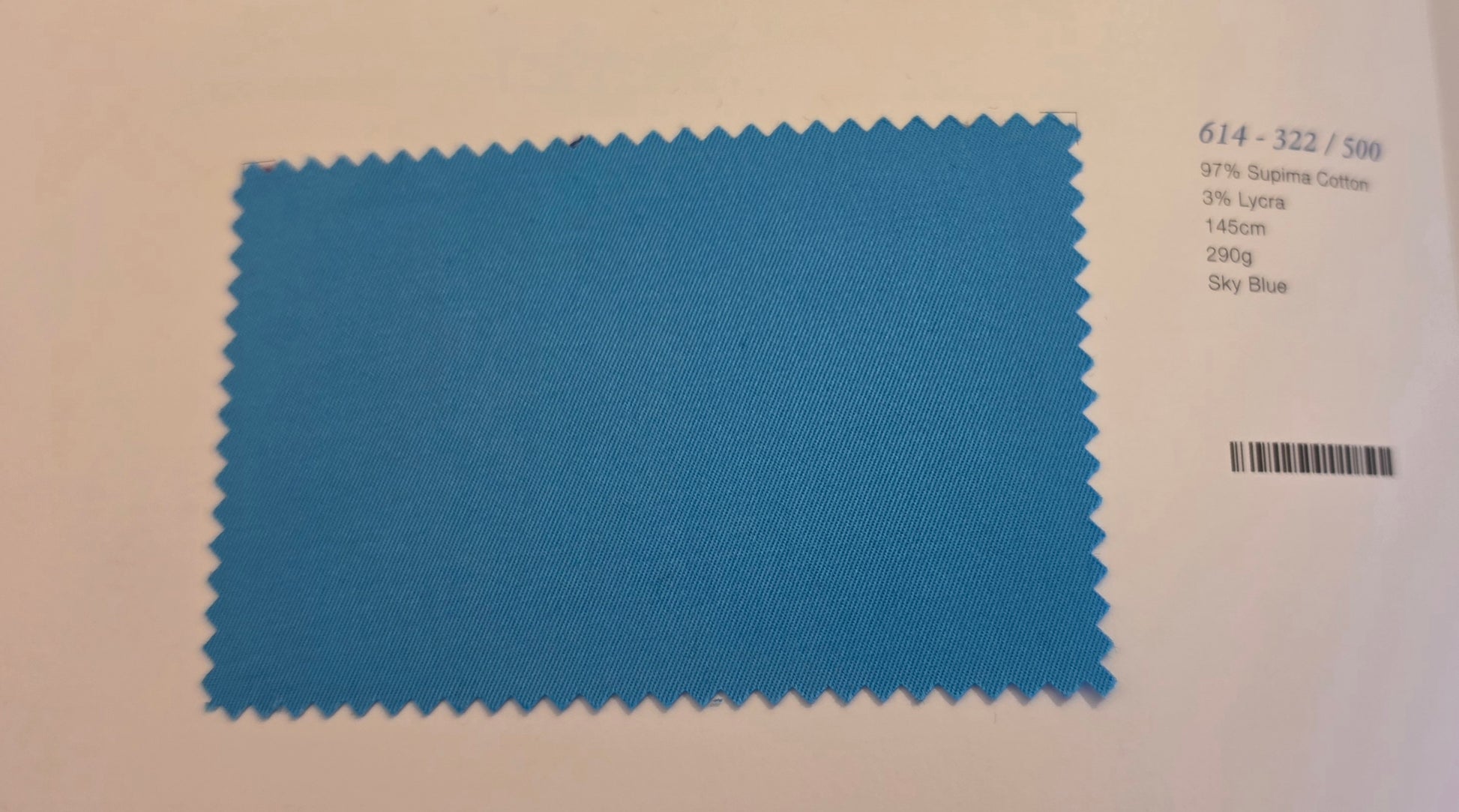 A blue fabric color swatch card with serrated edges, showing a textured sky blue material. To the right of the swatch, printed text identifies the color as 'Sky Blue' and lists other color codes and a barcode.