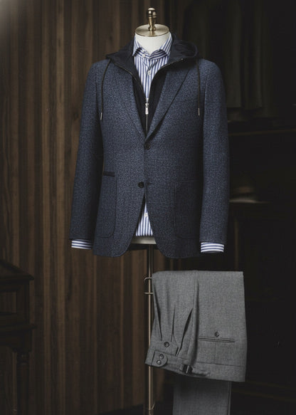 A blue textured casual single breasted jacket displayed on a mannequin with grey trousers, showcasing features such as a peaked lapel, front pockets, and a waistband side adjuster.