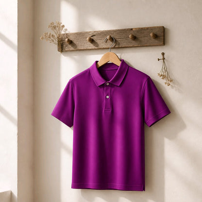 A bright purple short-sleeve polo shirt hanging on a wooden hanger from a rustic wooden wall hook rack, set against a warm beige wall with soft sunlight and shadows.