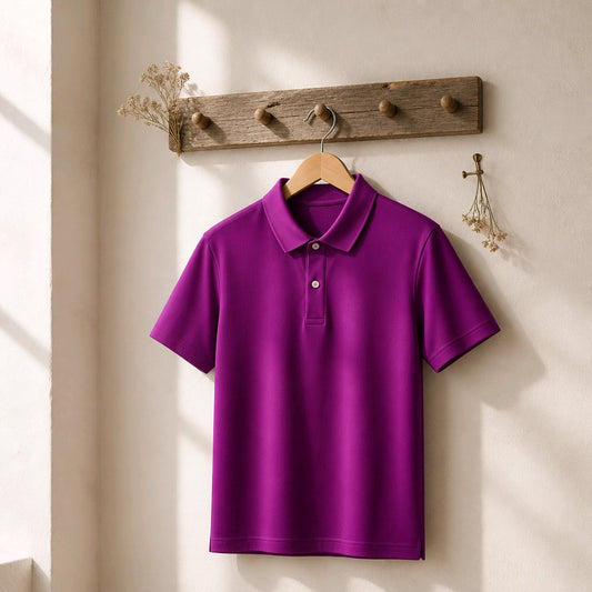 A bright purple short-sleeve polo shirt hanging on a wooden hanger from a rustic wooden wall hook rack, set against a warm beige wall with soft sunlight and shadows.