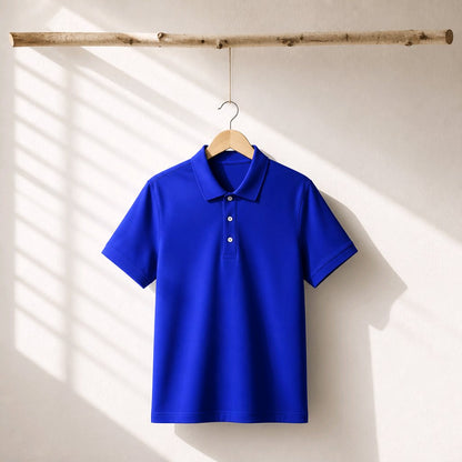 A bright royal blue short-sleeve polo shirt hanging on a wooden hanger from a rustic horizontal log, set against a warm off-white wall with soft diagonal window shadow patterns.