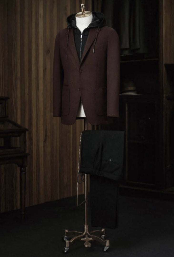 A burgundy check tweed jacket displayed on a mannequin with dark brown cord trousers, featuring a high shirt collar, front waistband, and cuffed sleeves.