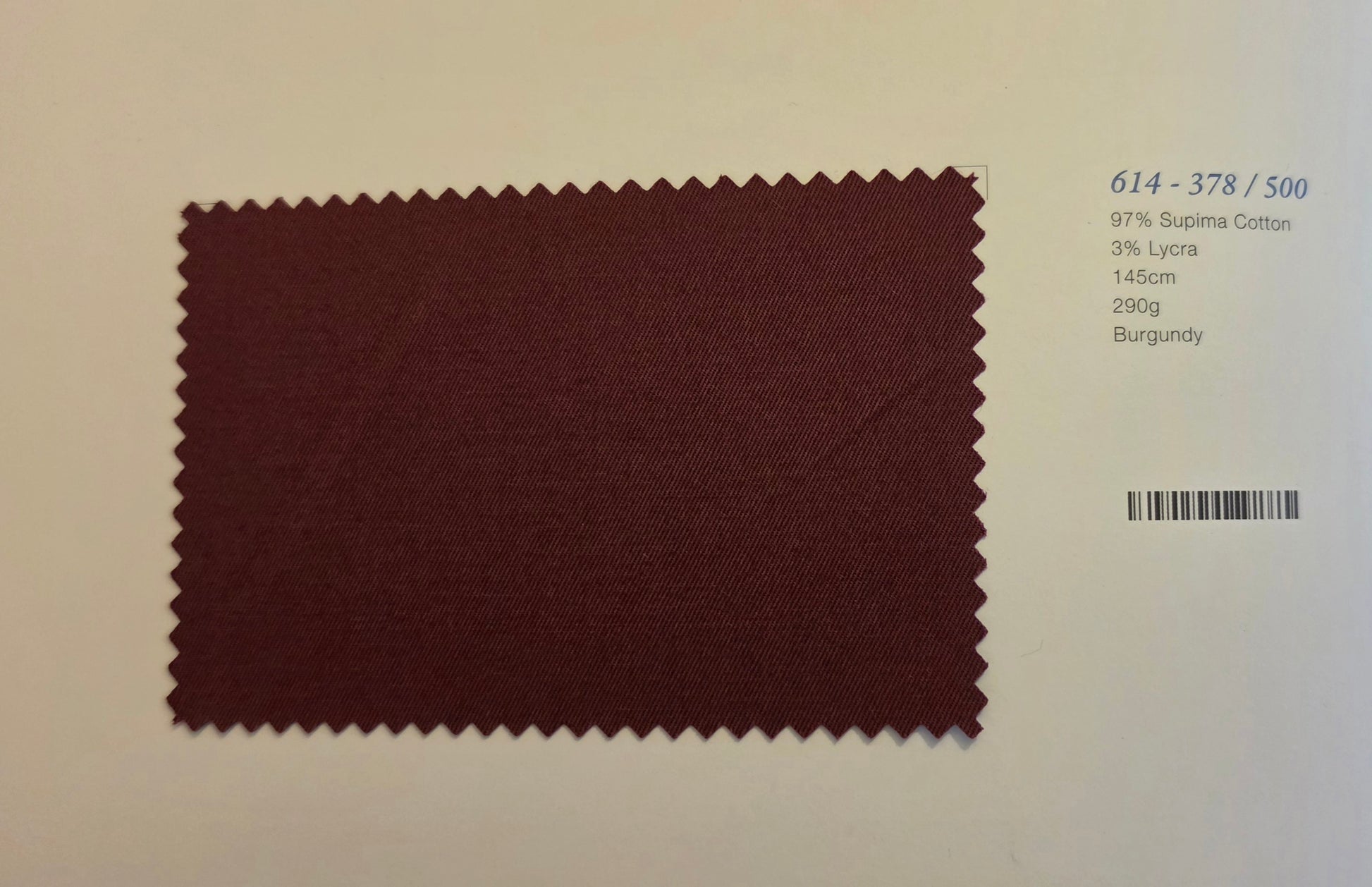 A burgundy fabric swatch with serrated edges displayed on a light beige background, next to printed text showing color and composition details.