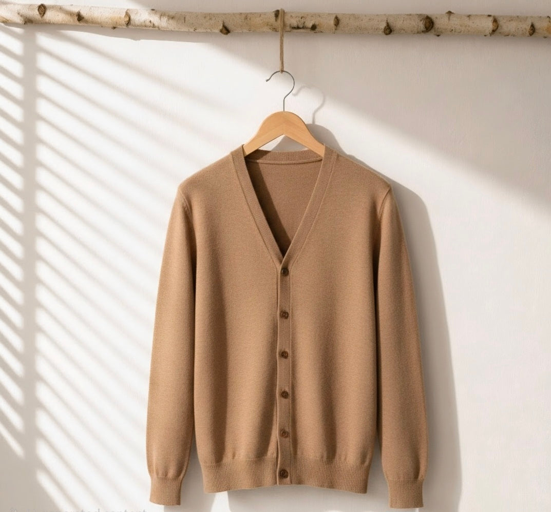 A camel brown knit cardigan sweater hanging on a wooden hanger against a white wall, with soft window shadow patterns cast across the background.