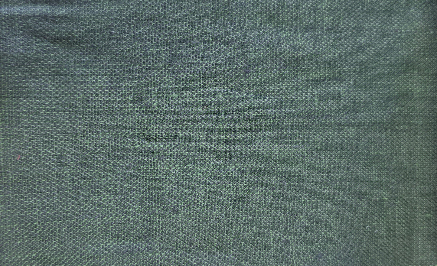 A close-up fabric swatch showing a dark green woven textile with a visible zigzag-cut fabric edge, alongside partial neighboring swatches in light wood and dark brown.
