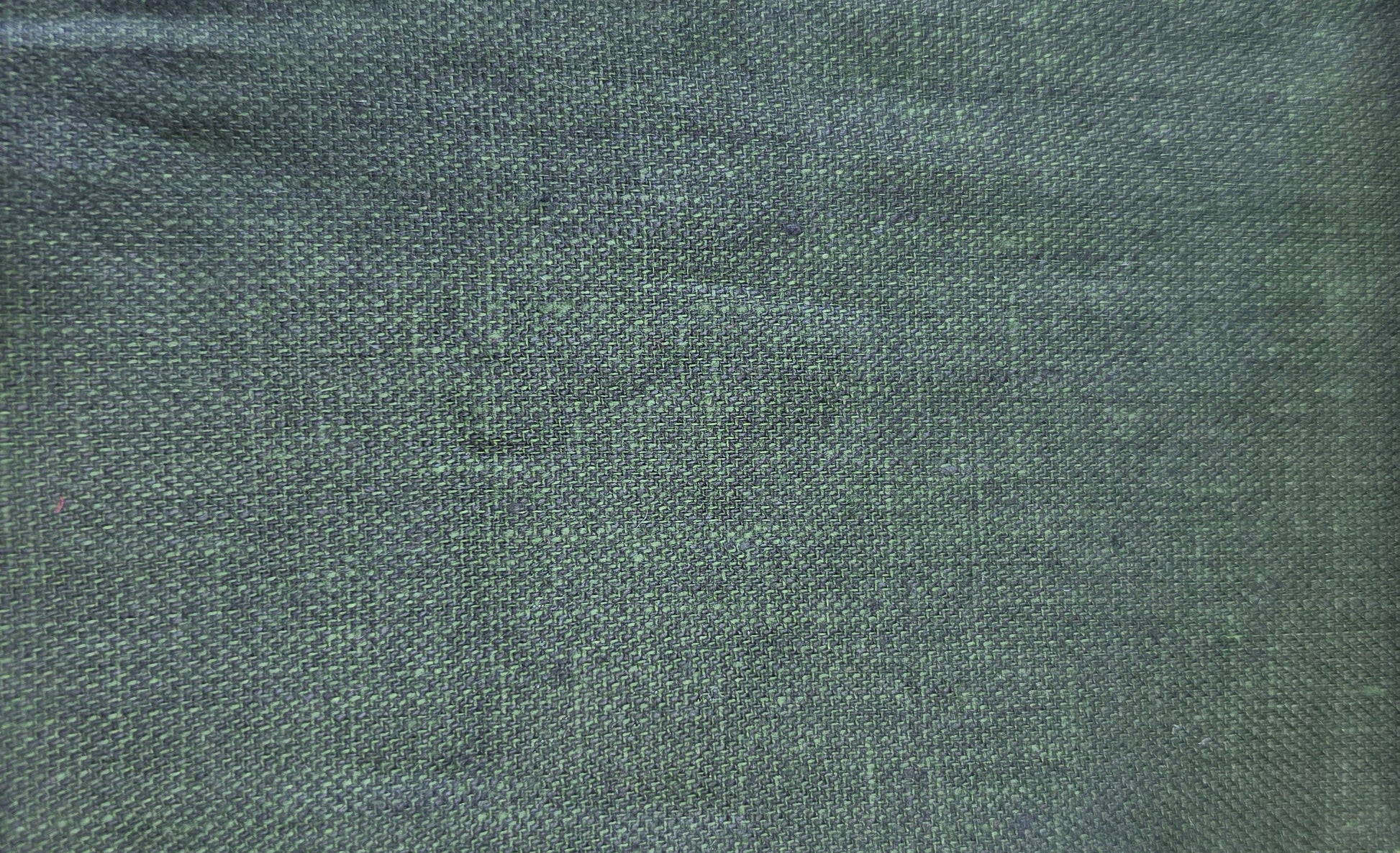 A close-up fabric swatch showing a dark green woven textile with a visible zigzag-cut fabric edge, alongside partial neighboring swatches in light wood and dark brown.