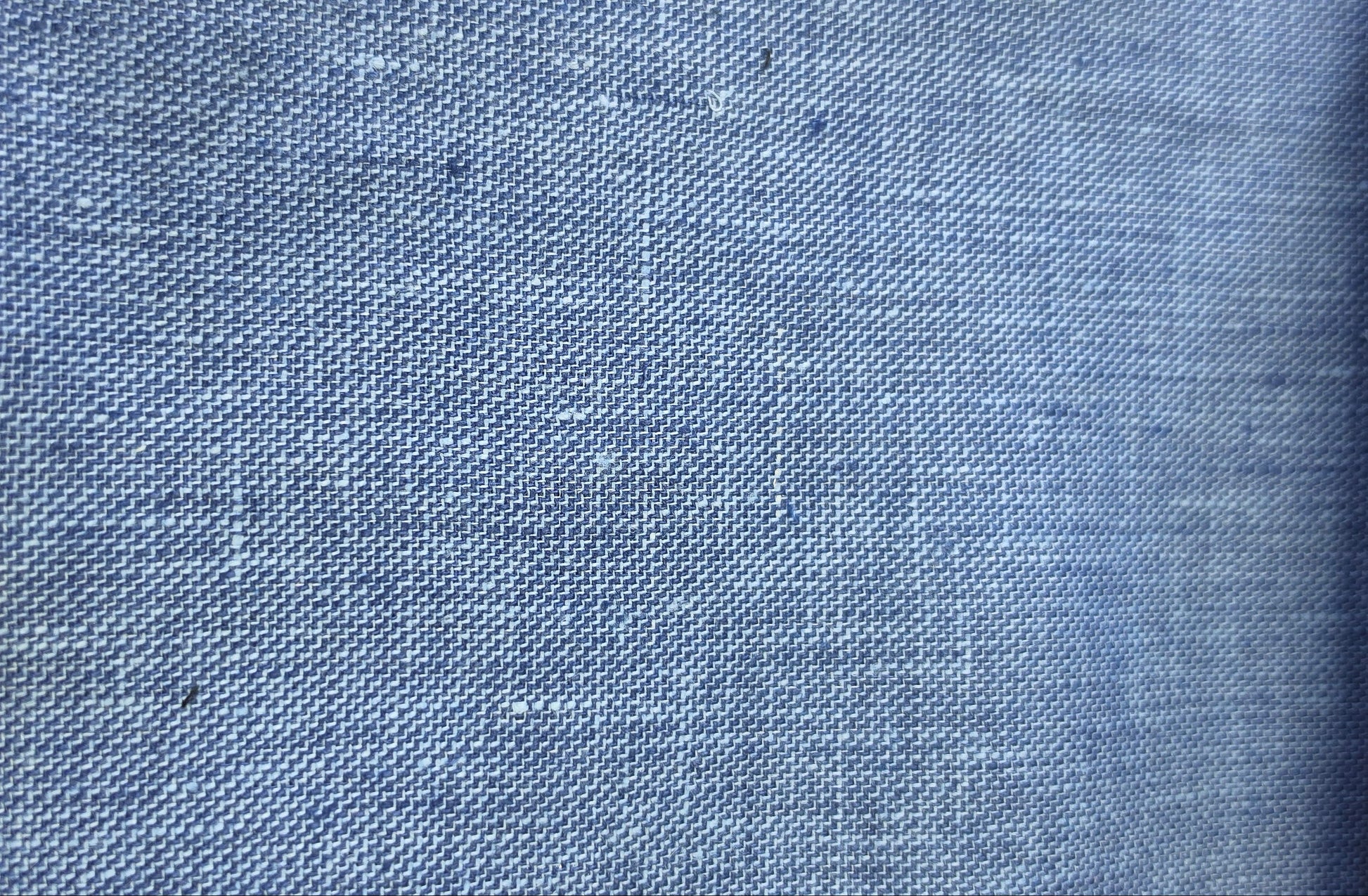 A close-up of a blue woven fabric texture with a subtle linen-like weave pattern.
