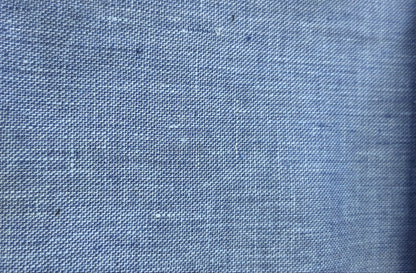 A close-up of a blue woven fabric texture with a subtle linen-like weave pattern.
