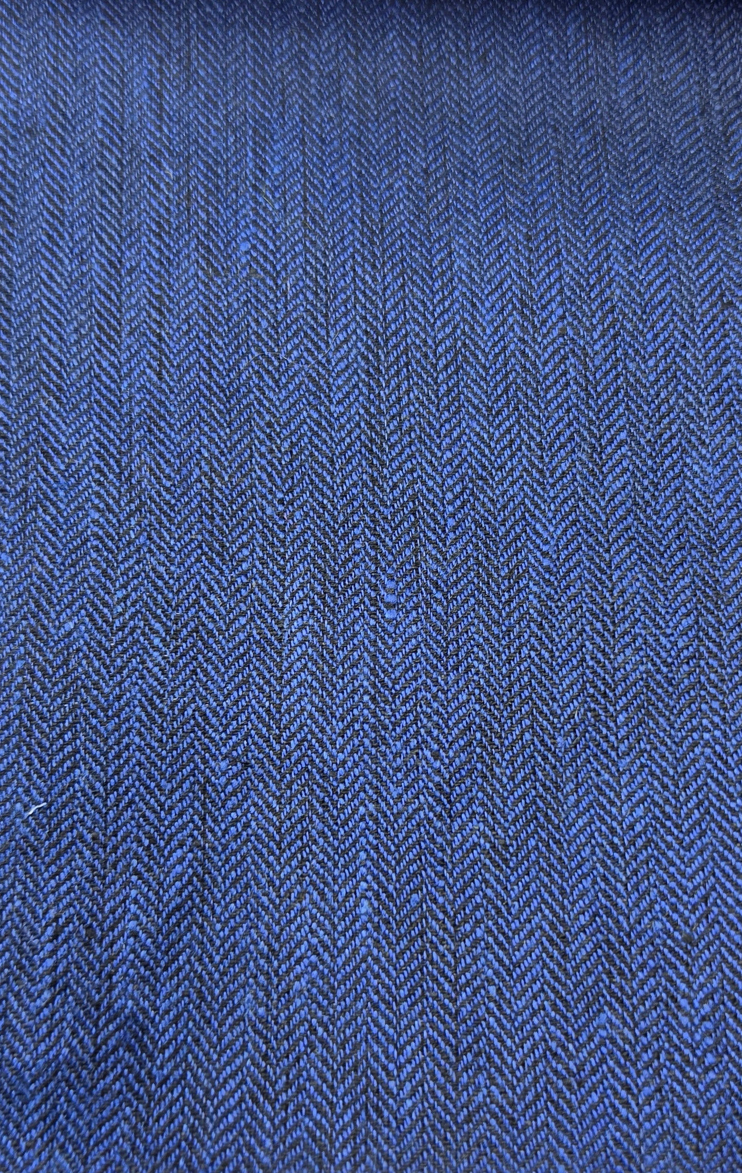 A close-up of a blue woven fabric with a visible herringbone texture, shown against a light wood background.