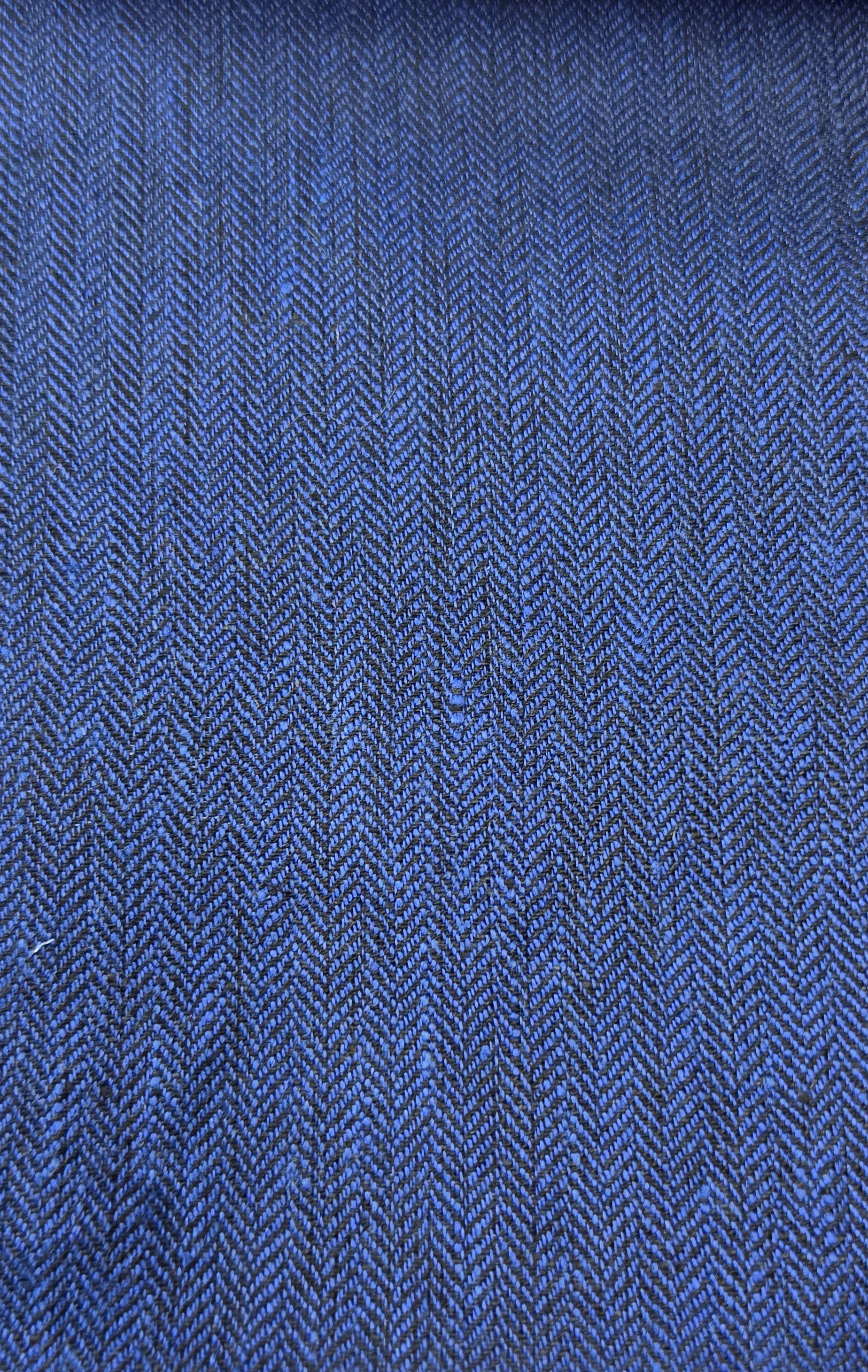 A close-up of a blue woven fabric with a visible herringbone texture, shown against a light wood background.