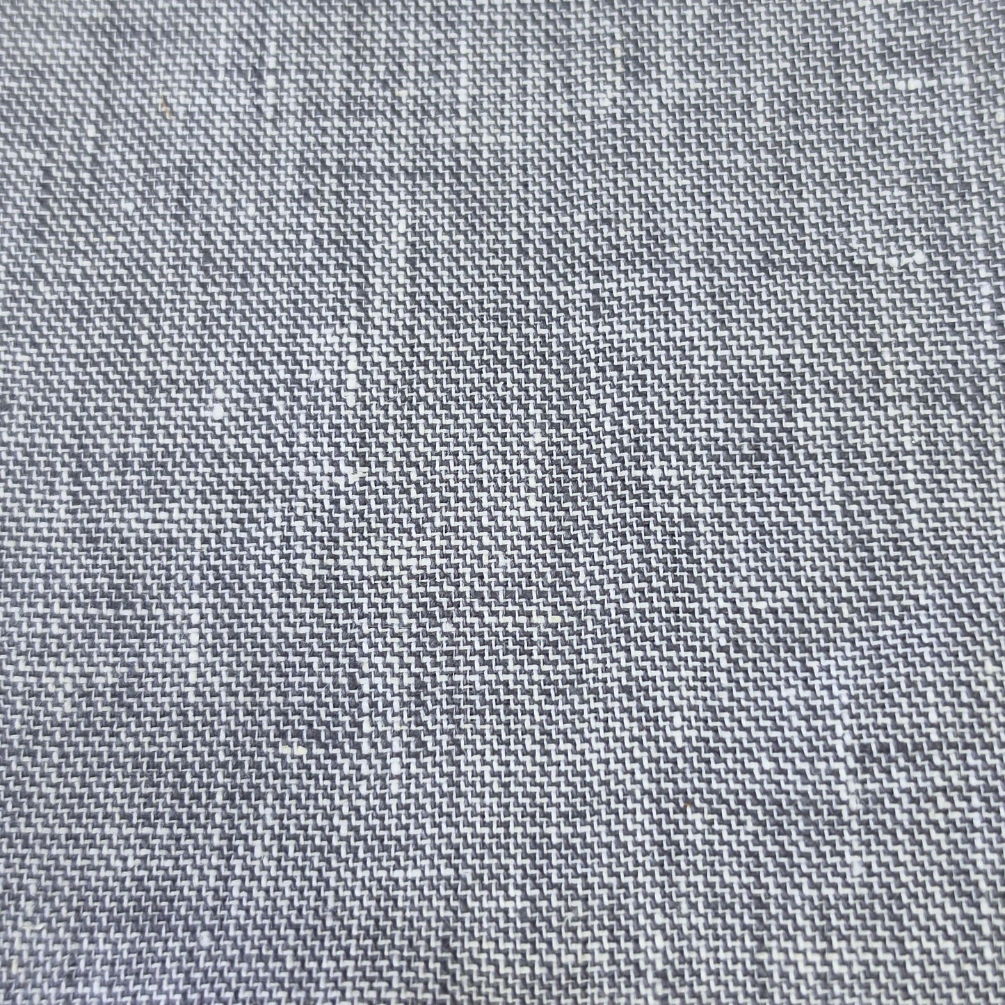 A close-up of a gray woven fabric sample with a textured linen-like pattern, showing the weave detail and a short stitched edge, resting on a wooden surface.