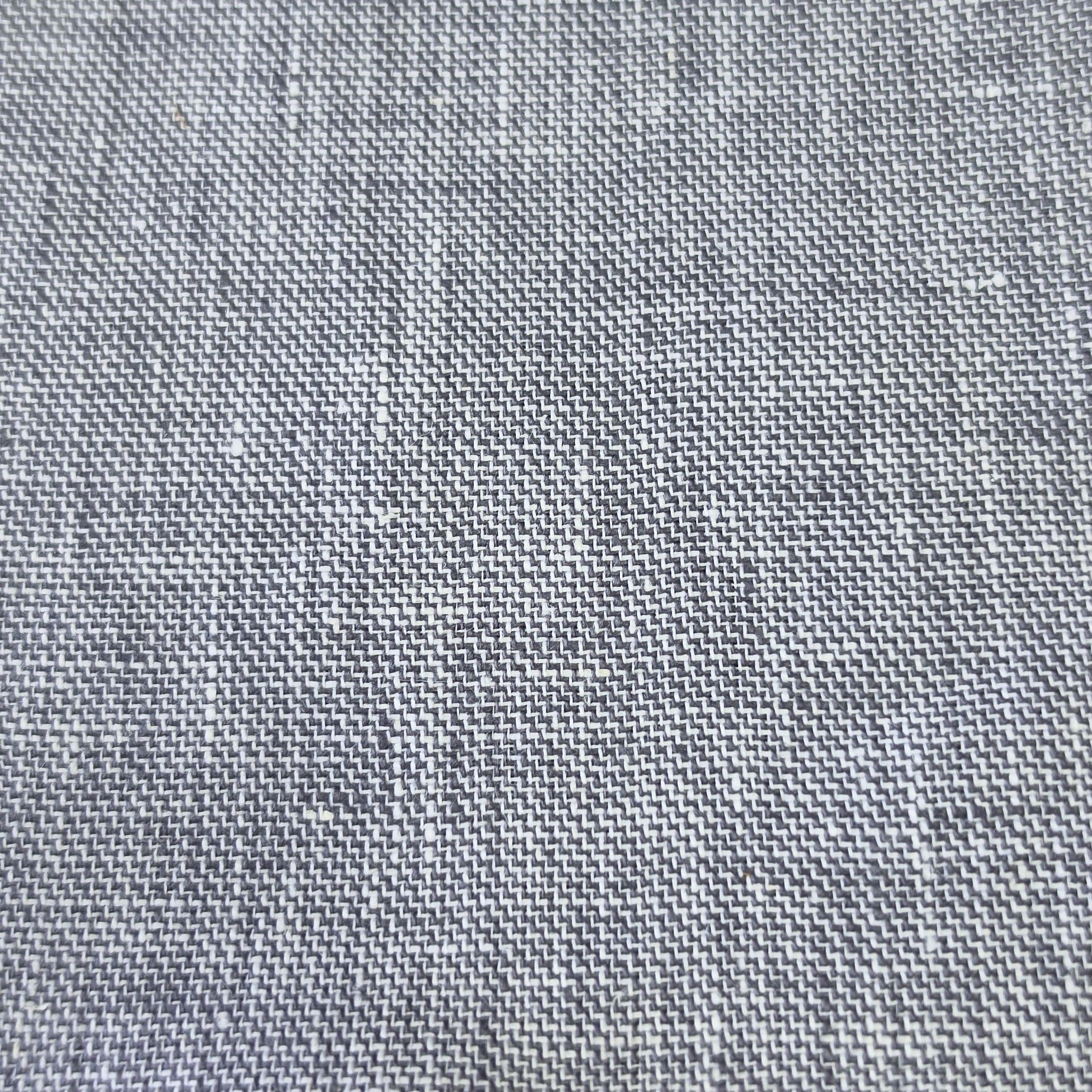 A close-up of a gray woven fabric sample with a textured linen-like pattern, showing the weave detail and a short stitched edge, resting on a wooden surface.