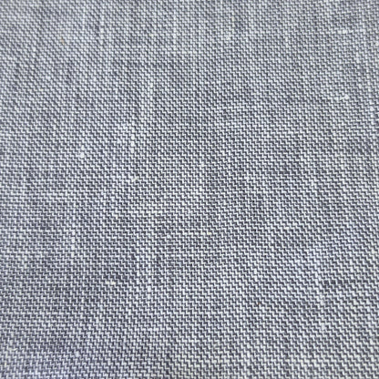 A close-up of a gray woven fabric sample with a textured linen-like pattern, showing the weave detail and a short stitched edge, resting on a wooden surface.