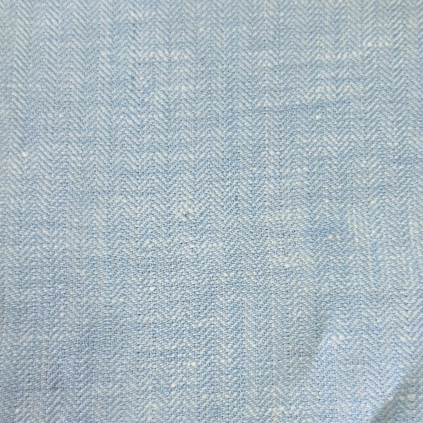 A close-up of a light blue and white herringbone patterned fabric, showing the woven texture and subtle folds.