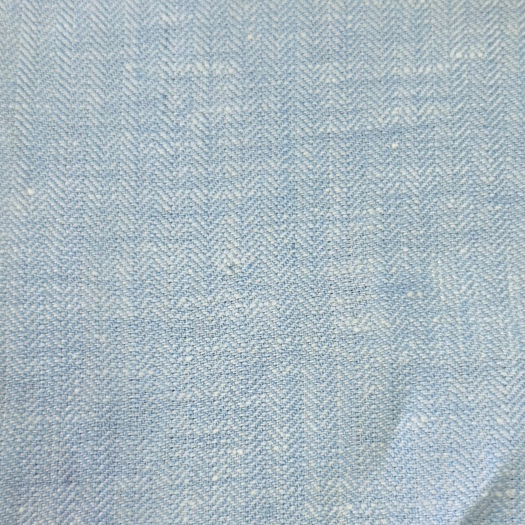 A close-up of a light blue and white herringbone patterned fabric, showing the woven texture and subtle folds.