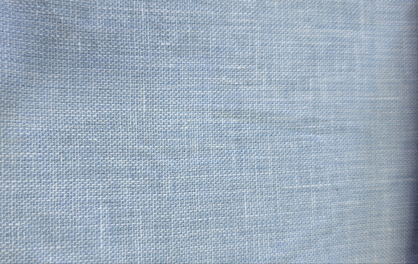 A close-up of a light blue woven fabric swatch with a visible zigzag stitched edge, shown against a neutral background.
