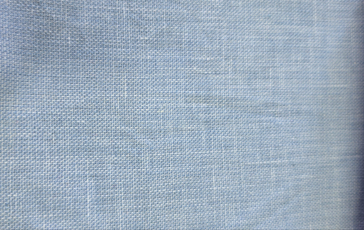A close-up of a light blue woven fabric swatch with a visible zigzag stitched edge, shown against a neutral background.