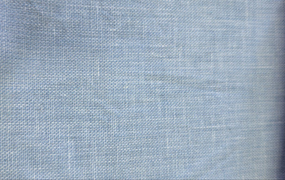 A close-up of a light blue woven fabric swatch with a visible zigzag stitched edge, shown against a neutral background.
