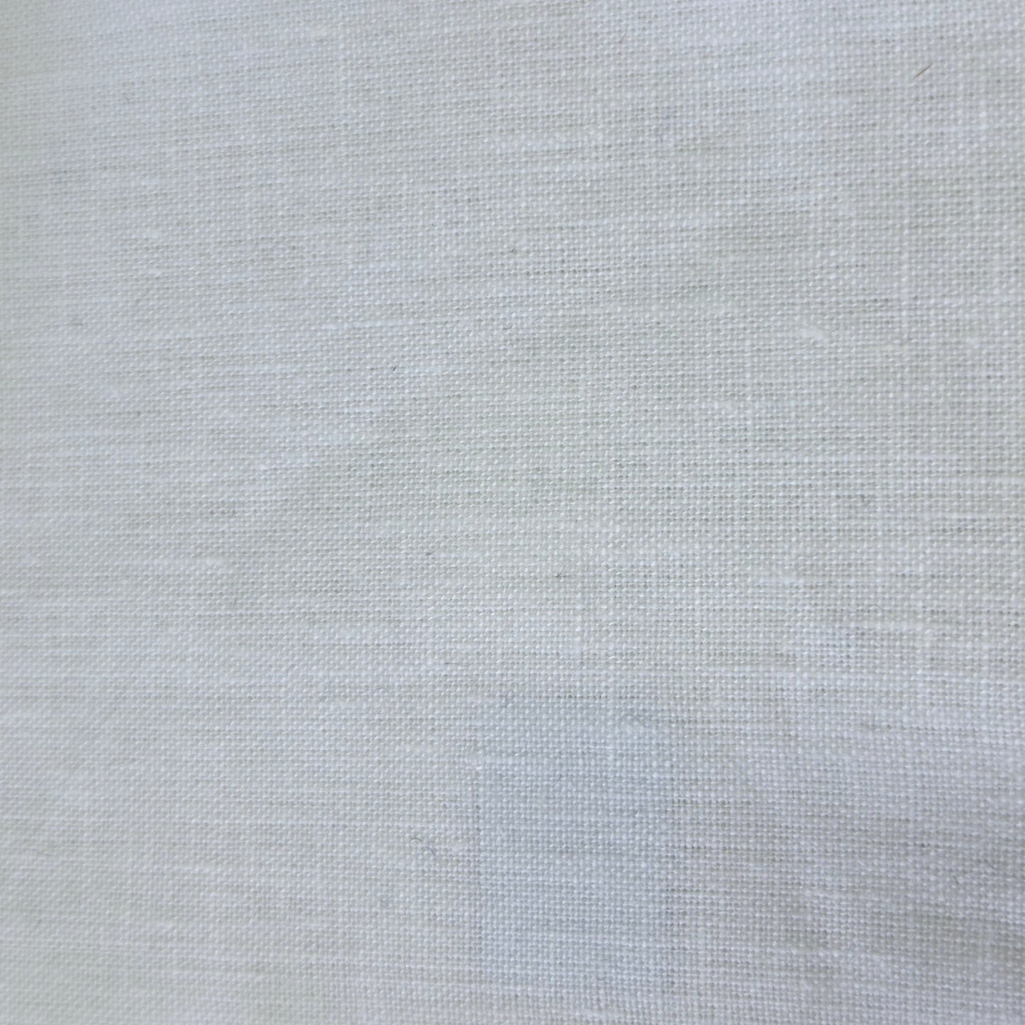 A close-up of a light gray woven fabric swatch with serrated edges, shown next to a dark textured material and a wooden surface.
