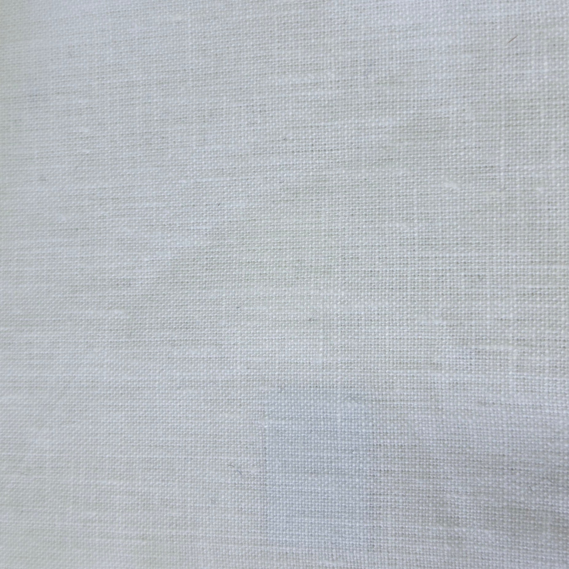 A close-up of a light gray woven fabric swatch with serrated edges, shown next to a dark textured material and a wooden surface.