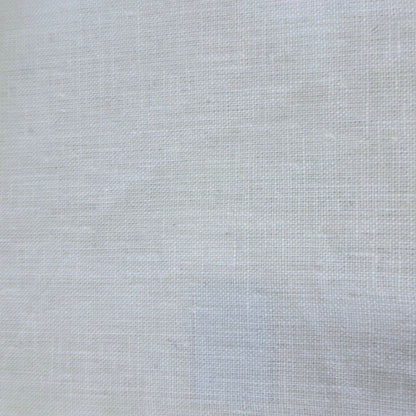 A close-up of a light gray woven fabric swatch with serrated edges, shown next to a dark textured material and a wooden surface.