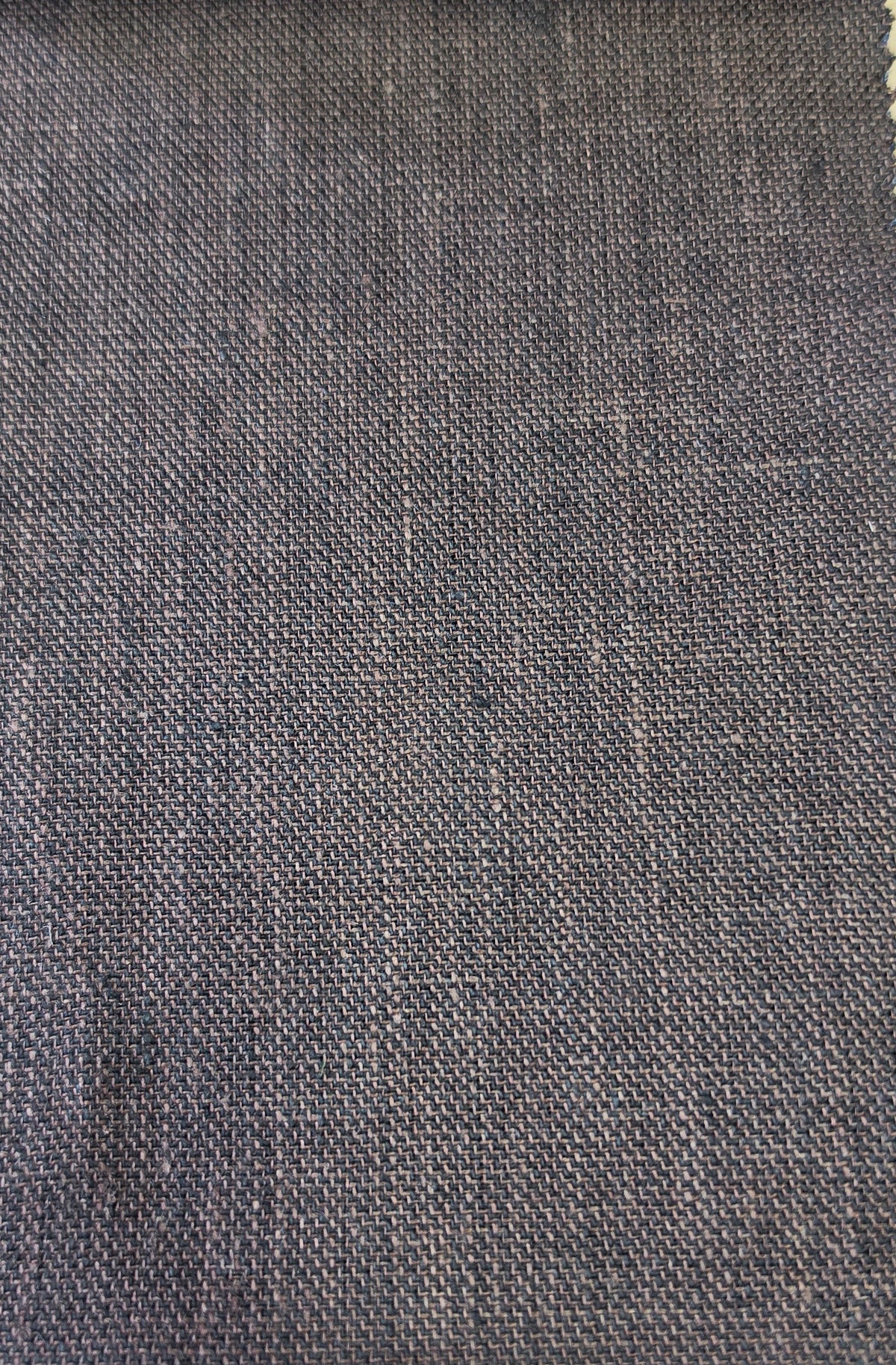 A close-up of a woven fabric swatch in a dark brown color, showing the texture and weave pattern, with a light wood surface visible at the bottom.