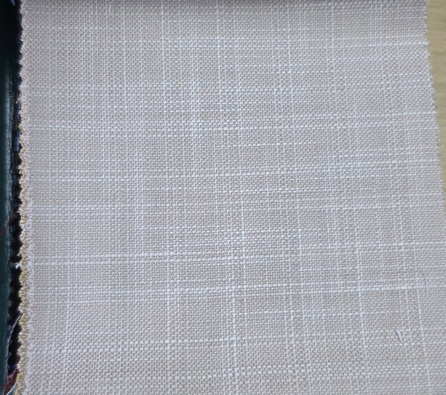 A close-up of a woven fabric swatch showing a light beige and white grid pattern, with a dark edge on the left and a tan edge on the right.