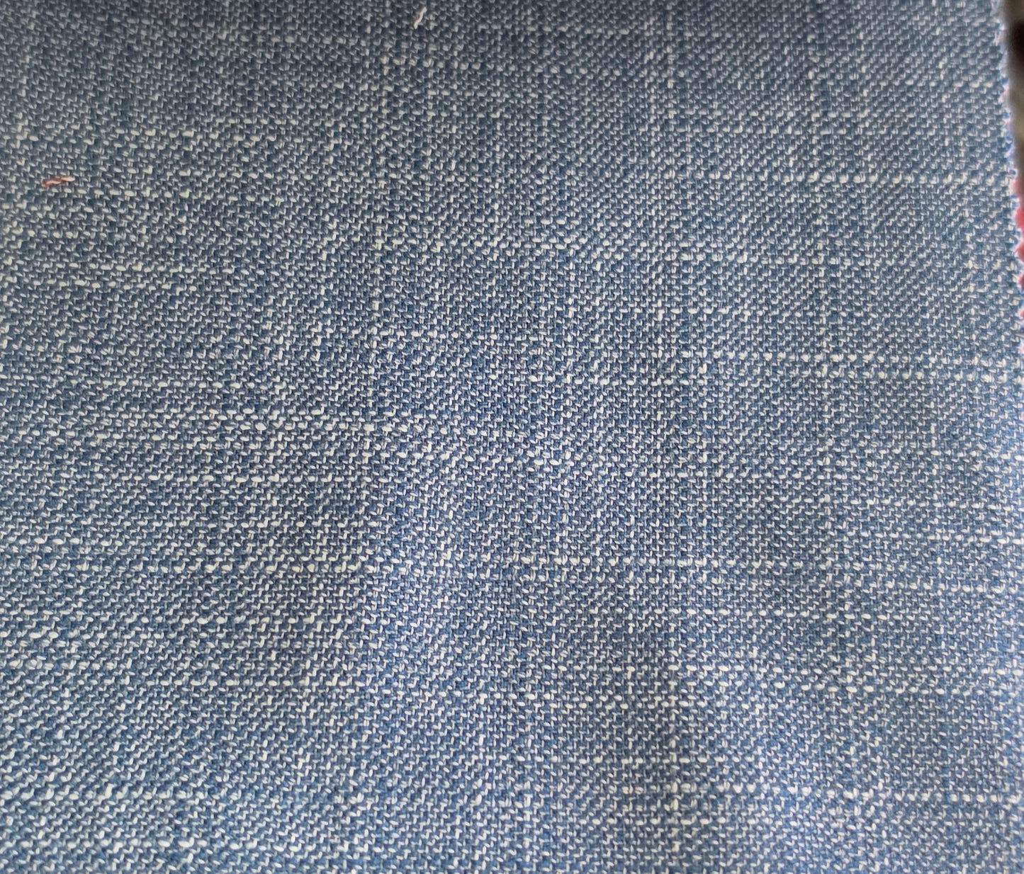 A close-up of a woven fabric texture in a dusty slate blue color with white threads forming a subtle grid pattern.