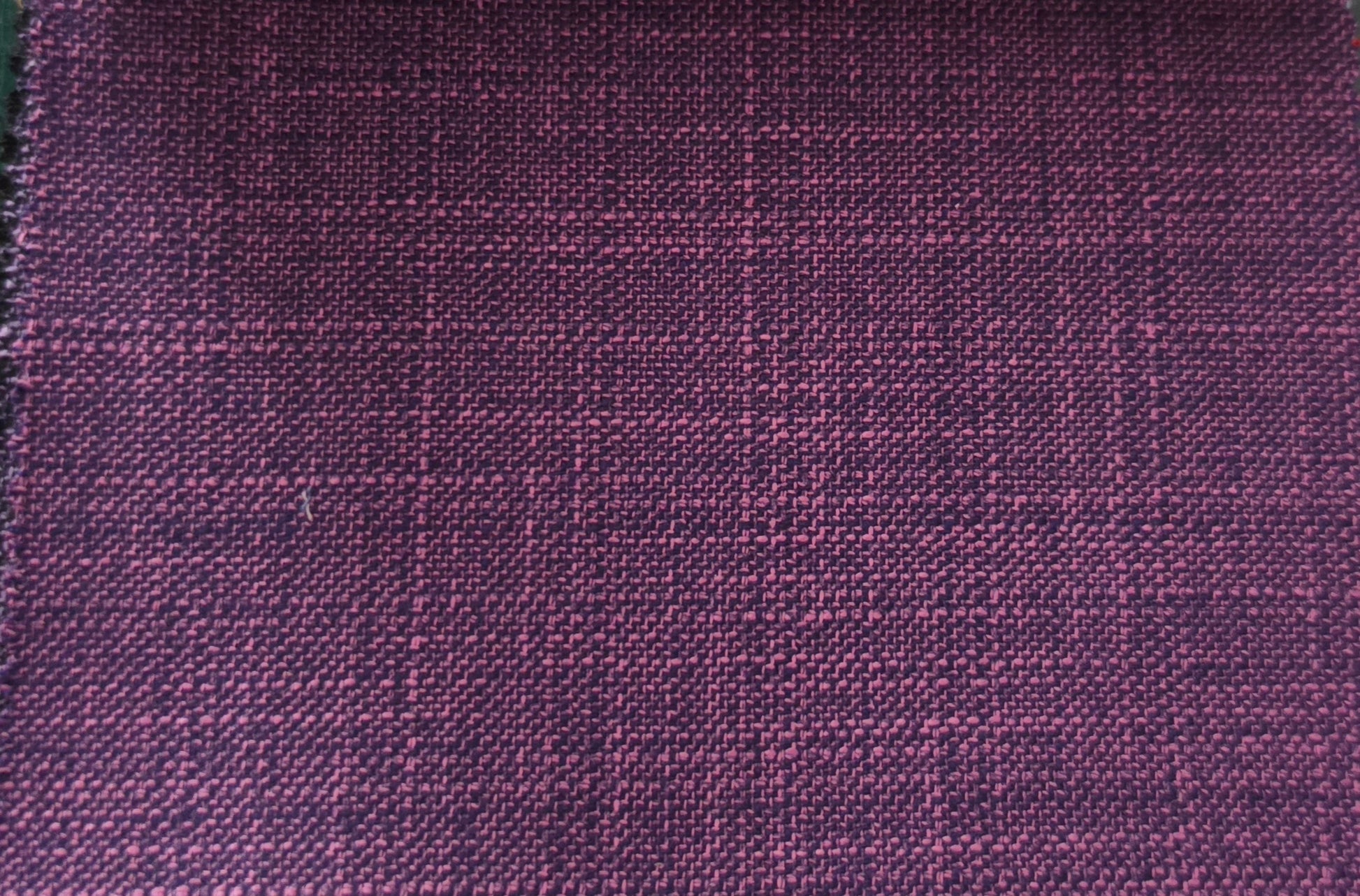 A close-up of a woven fabric with a subtle windowpane plaid pattern in deep purple and magenta tones.