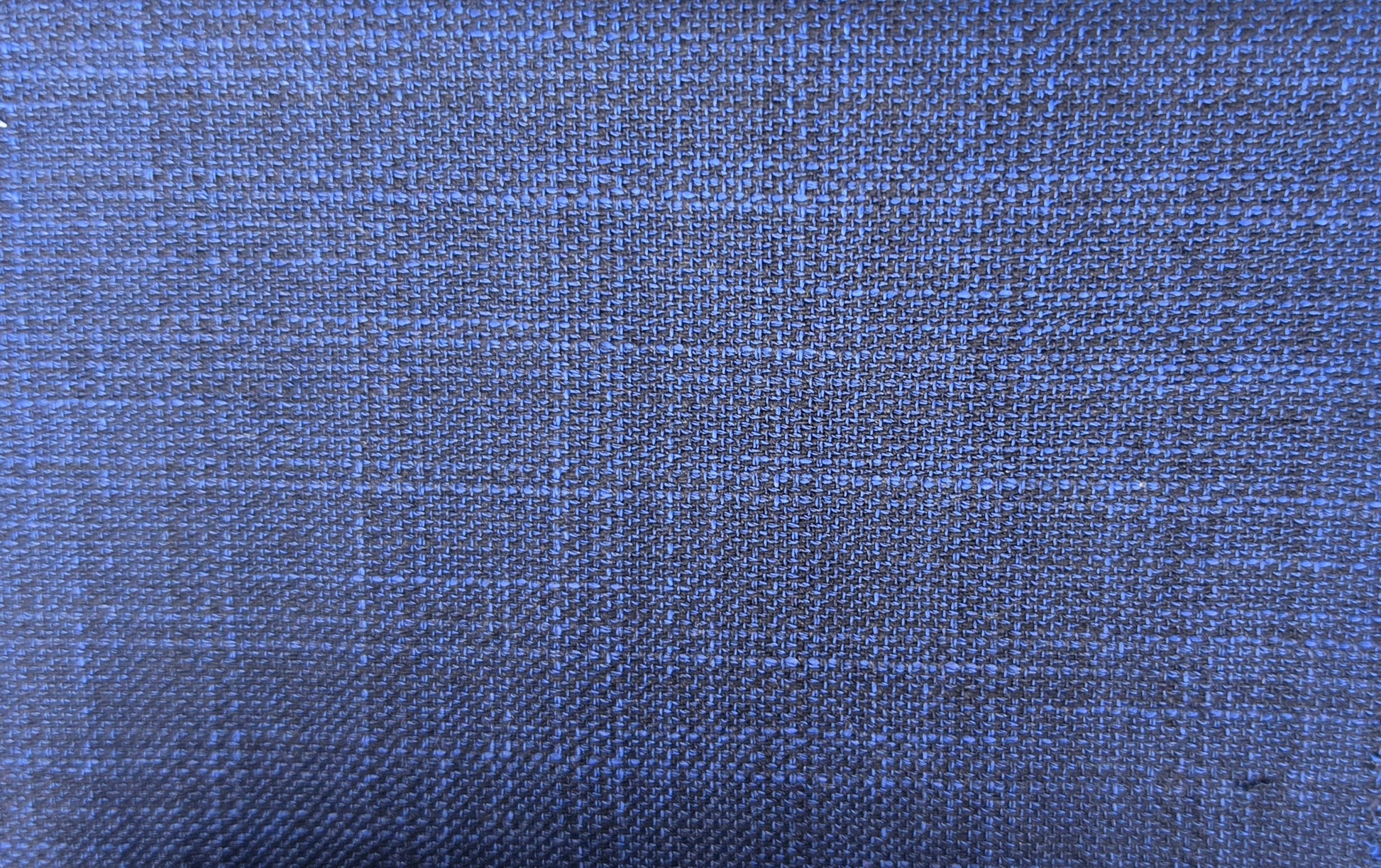 A close-up of woven fabric texture in a medium-to-dark blue color with subtle lighter blue and gray plaid lines.