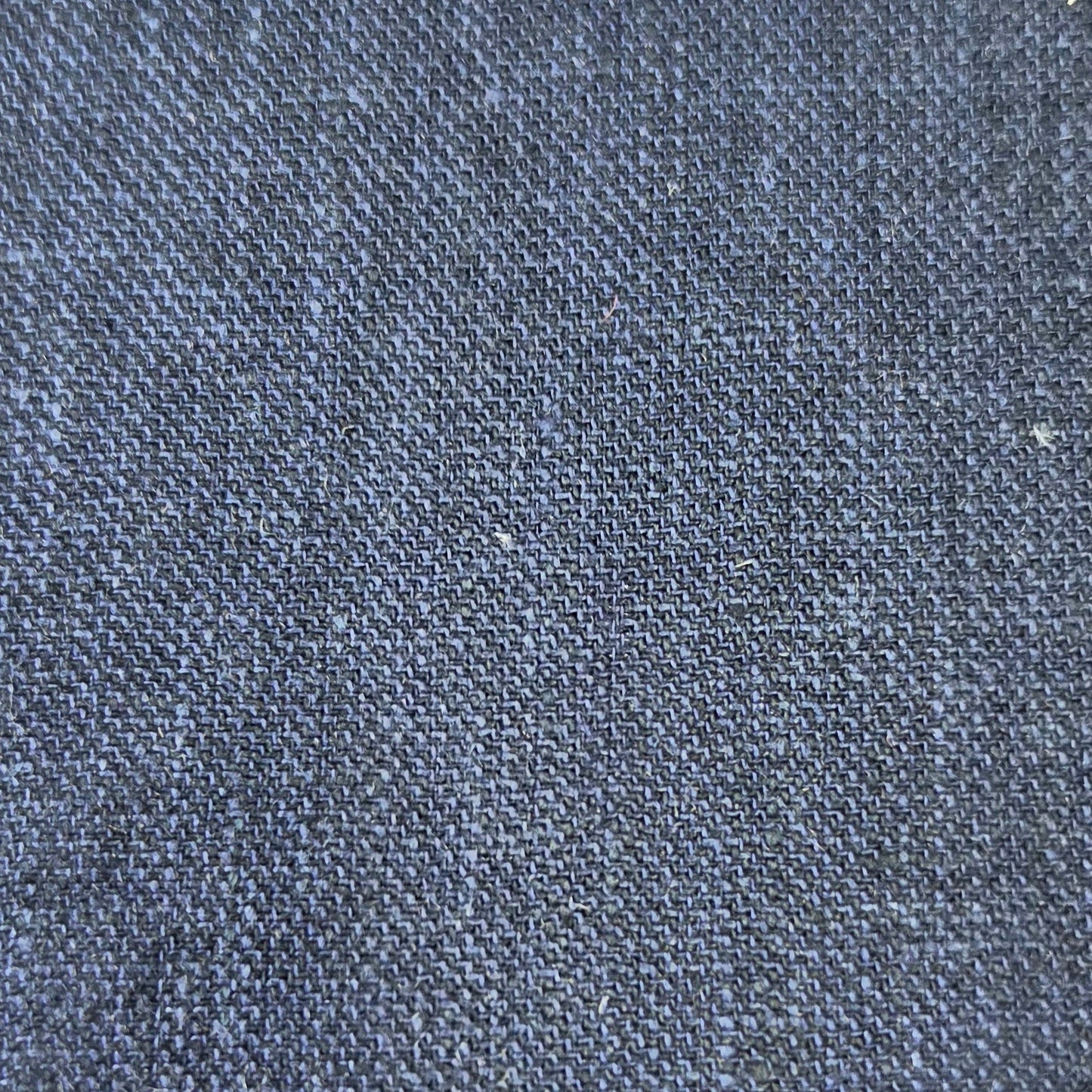 A close-up texture shot of dark indigo denim fabric, showing the detailed weave and subtle heathered blue and gray tones.