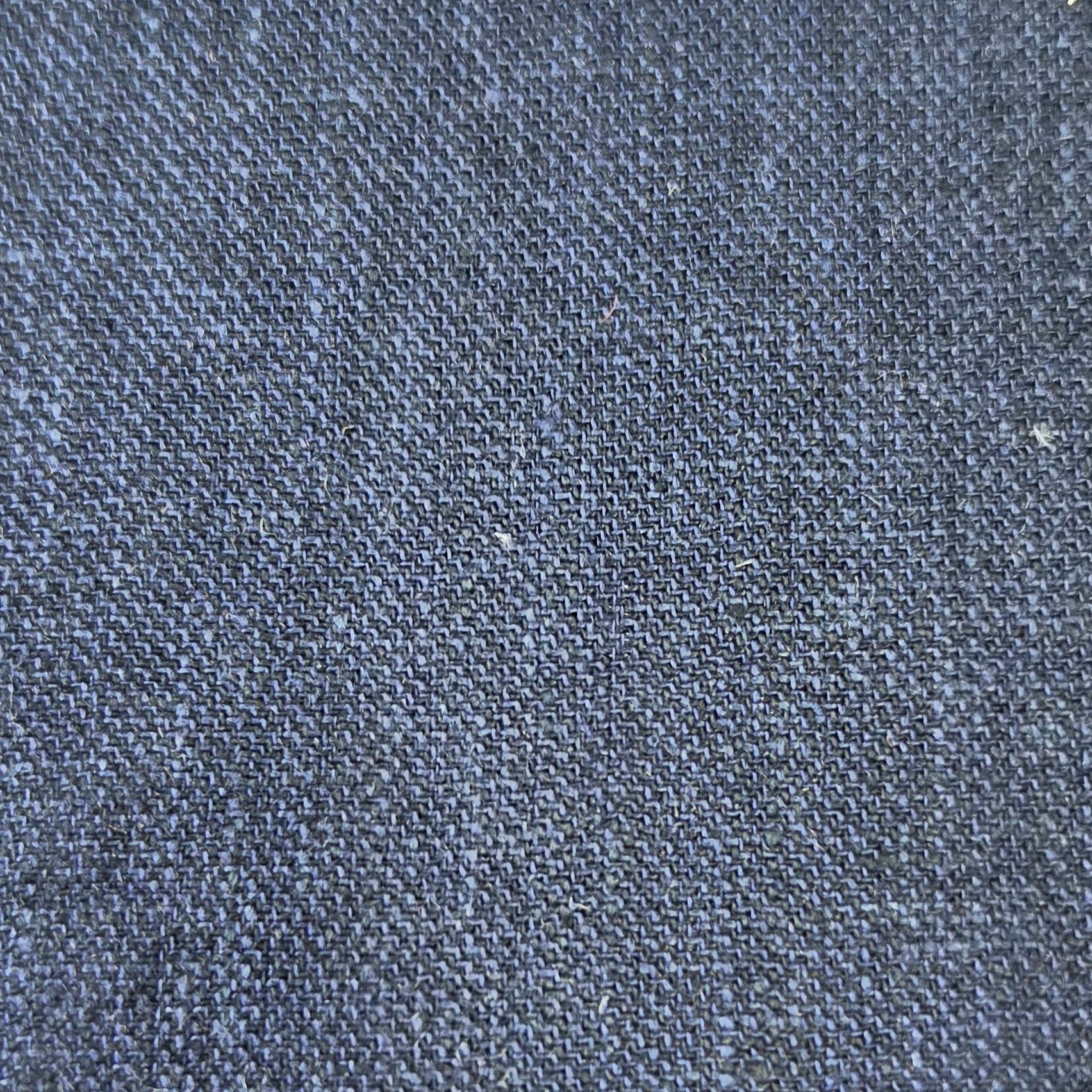 A close-up texture shot of dark indigo denim fabric, showing the detailed weave and subtle heathered blue and gray tones.